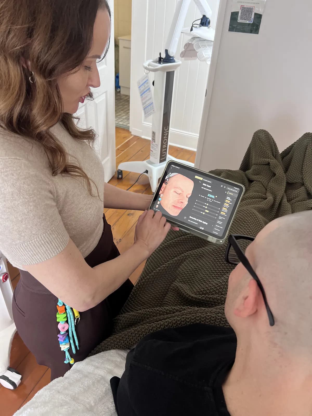 A practitioner reviews Ben's EVE MUSE skin analysis on a tablet beside the treatment bed.