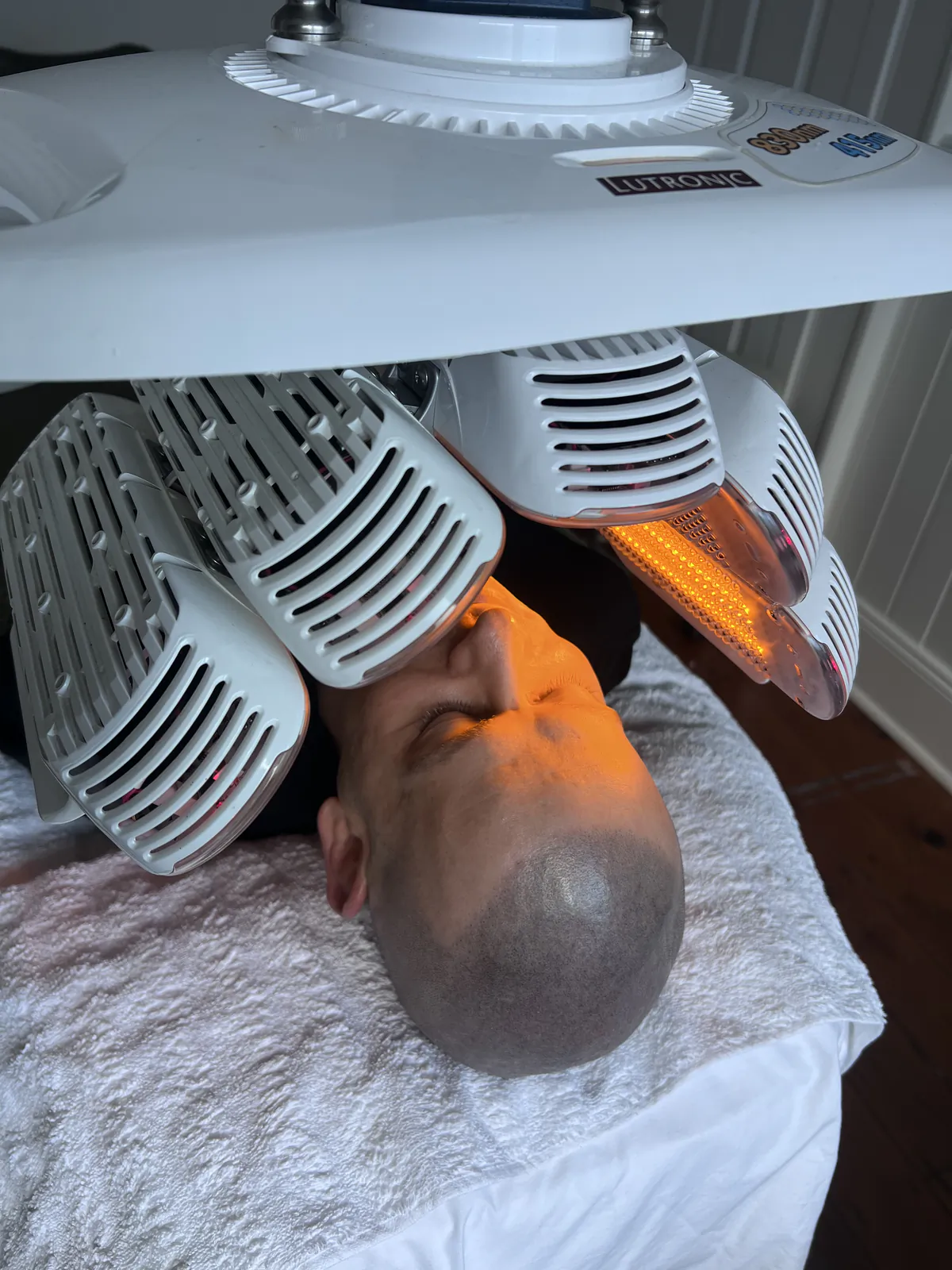 The LED light therapy array positioned over Ben's face while he lies on the treatment bed.